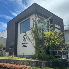 Modern two-story office building with dark gray framing, a white wall, large windows, and ivy climbing the facade near a MATIDA sign.
