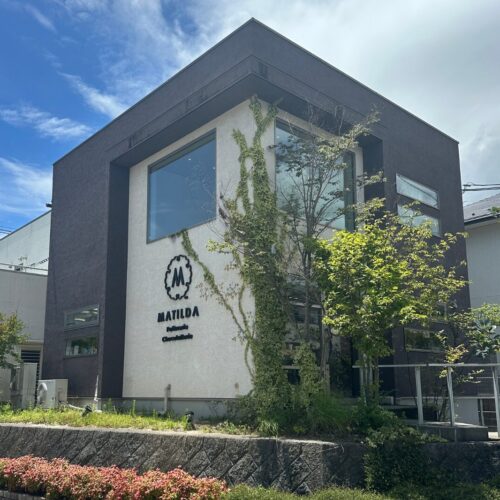 Modern two-story office building with dark gray framing, a white wall, large windows, and ivy climbing the facade near a MATIDA sign.