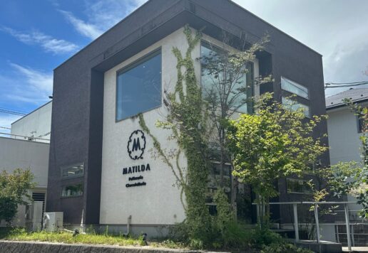 Modern two-story office building with dark gray framing, a white wall, large windows, and ivy climbing the facade near a MATIDA sign.