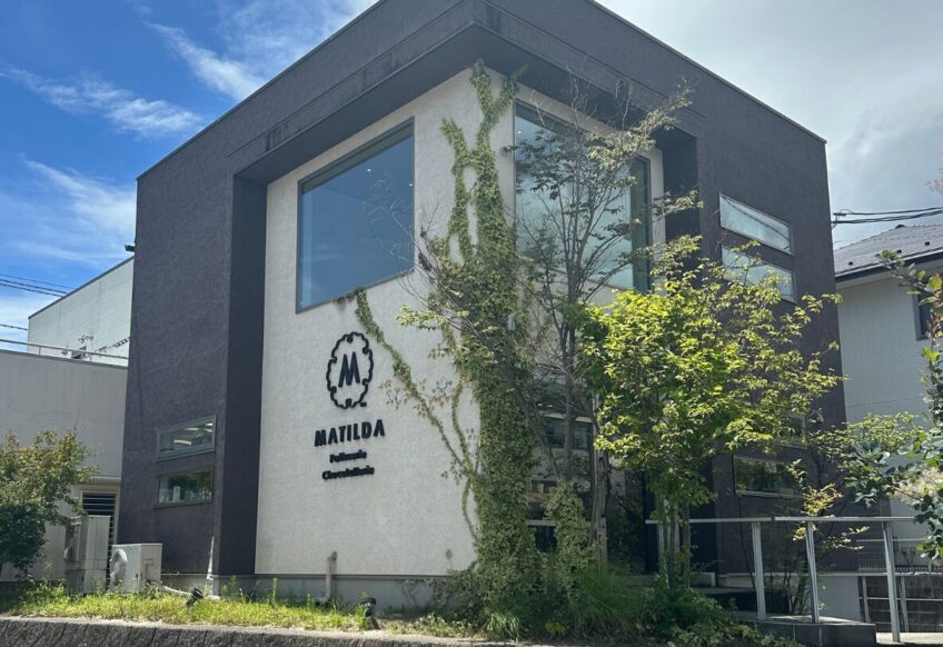 Modern two-story office building with dark gray framing, a white wall, large windows, and ivy climbing the facade near a MATIDA sign.