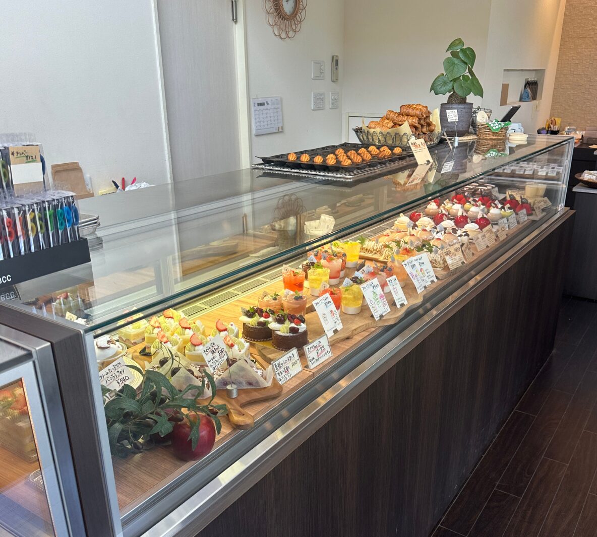 Glass bakery display case with assorted pastries and cakes arranged on a wooden counter inside a cafe.