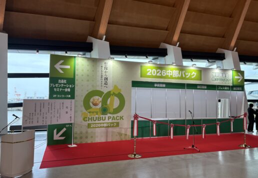 Exhibition booth area with green banners reading '2026 中部パック', red carpet, and a microphone stand in a convention hall.